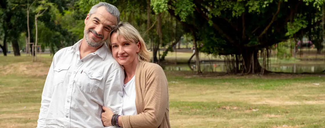 A middle aged couple smile together in a park