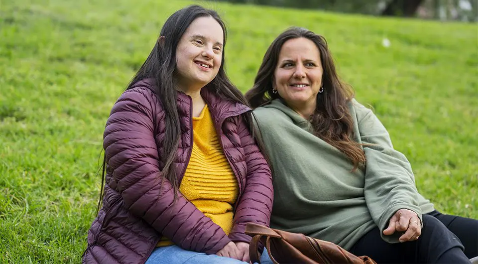 Two young woman sit together in a park.
