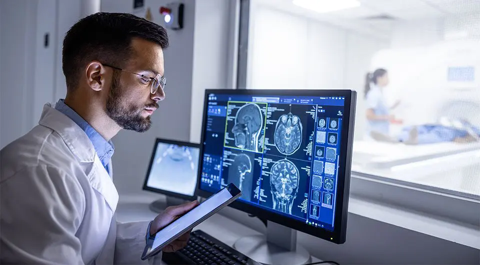 A scientist at a computer showing a brain scan.