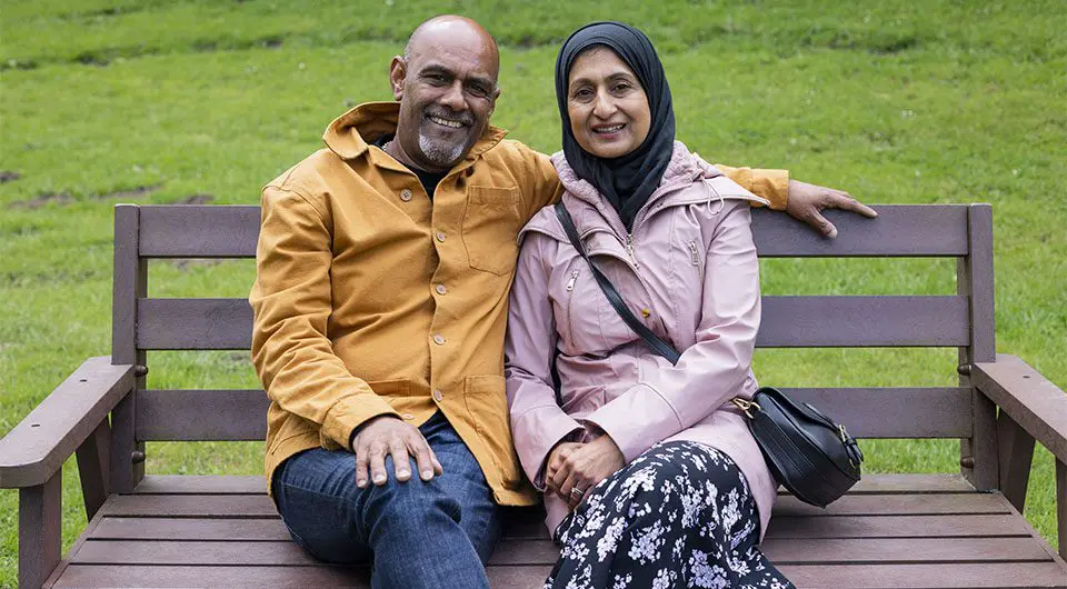 An older couple dressed for the autumn pose together on a park bench